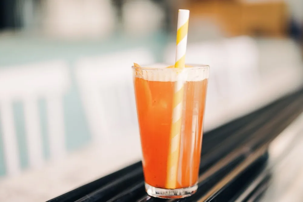 Bright orange cold drink served in a glass with a straw